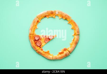 Vista dall'alto con la crosta e una fetta singola di pizza pepperoni. Vista dall'alto con avanzi di pizza su sfondo verde. Foto Stock