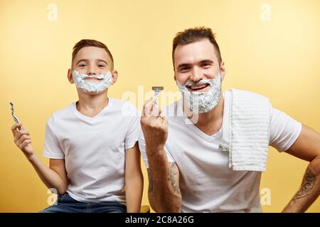 Paterne e figlio bearded che si rade su sfondo giallo Foto Stock