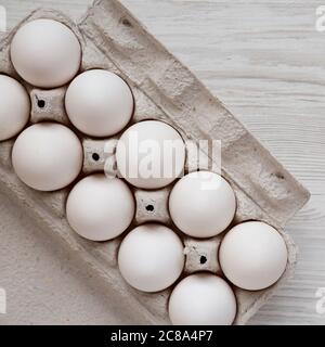 Uova bianche biologiche non cotte in una scatola di carta su sfondo bianco di legno, vista dall'alto. Posa piatta, sovratesta, dall'alto. Foto Stock