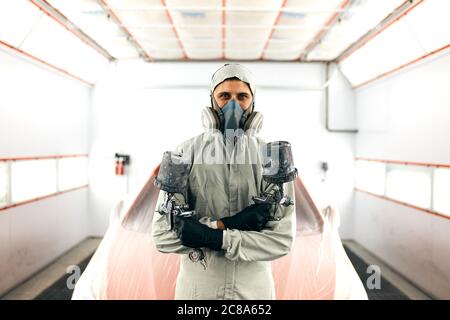 ritratto di un pittore meccanico di auto che indossa una maschera protettiva e vestiti in una camera di verniciatura Foto Stock