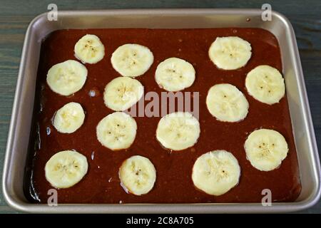 Batter di torta all'olio di oliva al cioccolato integrale gustoso e sano con Banana matura tagliata in una padella pronta per la cottura Foto Stock