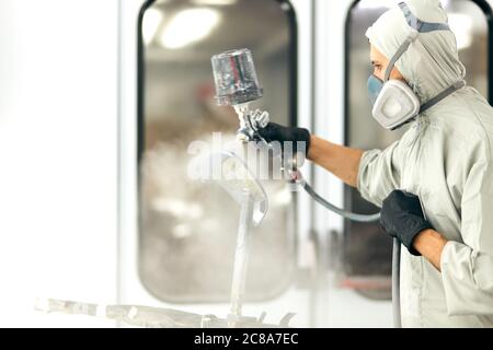 Uomo con indumenti protettivi e una maschera per la verniciatura auto del tetto usando il compressore Foto Stock