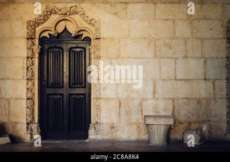 antica porta in legno attraverso la parete di pietra gialla del chiostro di un antico monastero portoghese con tradizionali modelli tardo gotici manuelini a. Foto Stock