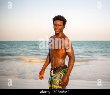 Giovane attraente muscoloso e forte atletico Black African Man sorridente alla spiaggia di sabbia bianca Foto Stock