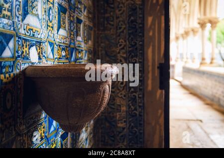 antica pietra fonte d'acqua santa in una cappella di un monastero portoghese medievale, decorata con tradizionali piastrelle dipinte blu Foto Stock