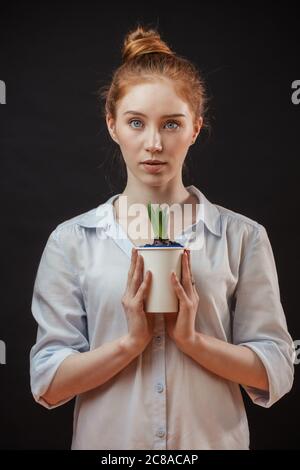 Giovane donna dai capelli rossi con nodo per capelli che tiene in vaso pianta isolato obero sfondo nero Foto Stock