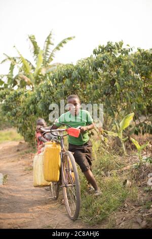 I bambini usano una bicicletta per prendere e trasportare acqua in un villaggio rurale nel distretto di Rakai, Uganda, Africa orientale. Foto Stock