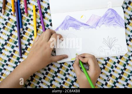 Inquadratura ad alto angolo di una persona che disegnano montagne su un carta bianca con matite colorate Foto Stock