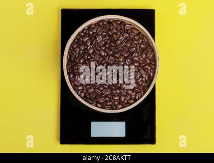 Recipiente in legno con chicchi di caffè su scala nera su sfondo giallo. Foto Stock
