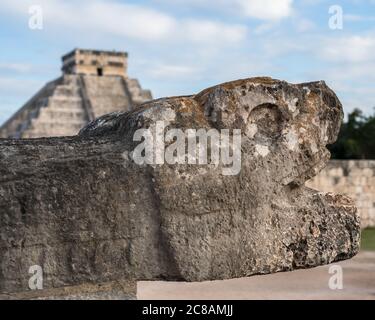 Una testa di pietra scolpita giaguaro al campo da ballo grande nelle rovine della città maya di Chichen Itza, Yucatan, Messico. Dietro c'è il Grande Pirami Foto Stock