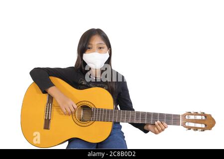 Una studentessa asiatica che indossa una maschera e suona la chitarra a casa.l'immagine mostra l'idea durante la quarantena domestica per ridurre la diffusione della corona Foto Stock