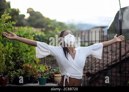 Giovane donna nera in maschera facciale apre le braccia e si rilassa in balcone Foto Stock