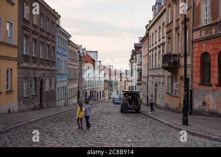 Varsavia / Polonia - 10 giugno 2019: Due bambini giocano su una strada acciottolata nel centro storico di Varsavia con vecchi edifici colorati Foto Stock