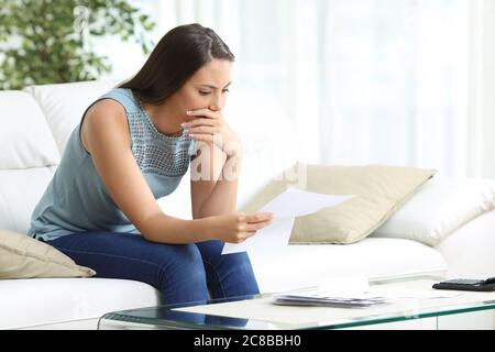 Donna preoccupata che legge lettter seduto nel divano nel soggiorno di casa Foto Stock