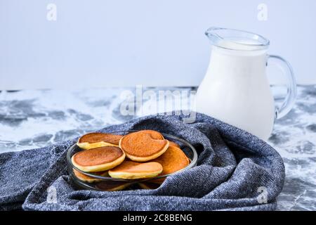 Porridge con pancake, mini pancake in un recipiente con sciroppo d'acero. Latte sullo sfondo. I mini pancake olandesi sono chiamati frittelle di patate alla fragola. Foto Stock