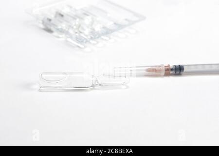 flaconcino e siringa di vetro medico su sfondo bianco del tavolo con ombra. Foto Stock