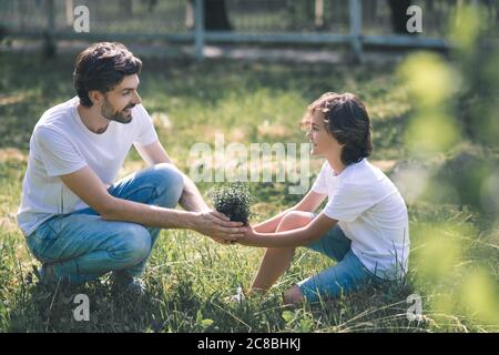 Ragazzo dai capelli scuri e suo padre che tiene la pianta e sorride Foto Stock