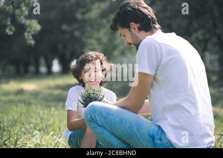 Ragazzo dai capelli scuri sorridendo e tenendo la pianta, suo padre seduto accanto a lui Foto Stock