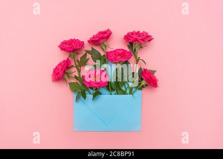 Busta blu pastello piena di fiori rosa su sfondo rosa. Disposizione piatta. Biglietti di invito per matrimoni o lettera d'amore. San Valentino o altre vacanze. Foto Stock