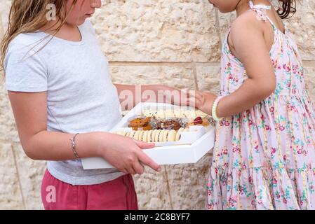 Giovane donna, ragazza adolescente carina che consegna a casa i dolci diversi in una scatola bianca. Il bambino piccolo raggiunge per i biscotti. Foto Stock