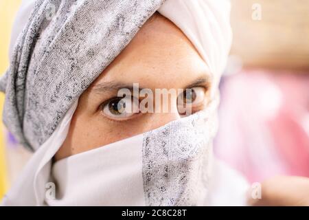 Donna caucasica vestita con un tradizionale abito berbero che copre il viso mentre si affaccia sulla fotocamera. Concetto di viaggio in Marocco Foto Stock
