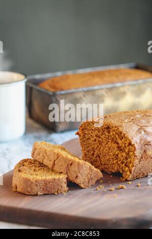 Pane di zucca appena sfornato su un tagliere con caffè caldo in background. Foto Stock