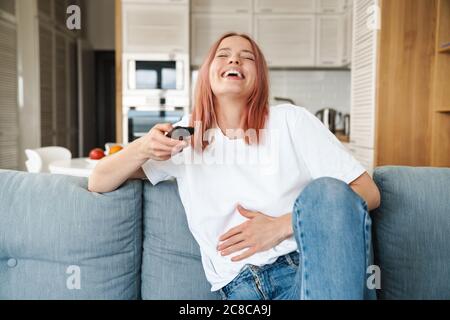 Bella giovane allegra bella donna che si rilassa su un divano nel soggiorno, guardando la tv Foto Stock