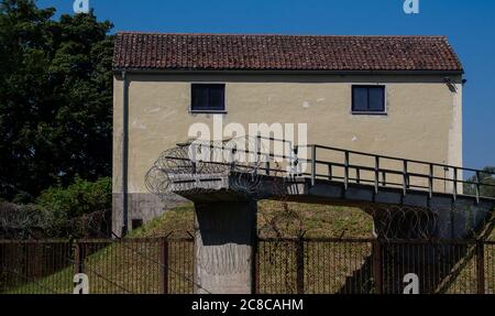 Un ponte di taglio fissato saldamente con filo dentellato contro l'ingresso. Sullo sfondo una vecchia casa. Foto Stock