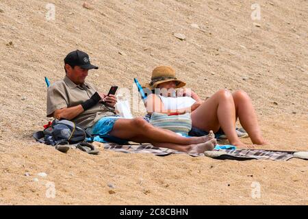 West Bay, Dorset, Regno Unito. 23 luglio 2020. Regno Unito Meteo. Una coppia di relax sulla spiaggia che è molto più tranquilla oggi presso la località balneare di West Bay in Dorset in una giornata nuvolosa con occasionali incantesimi di sole. Immagine: Graham Hunt/Alamy Live News Foto Stock