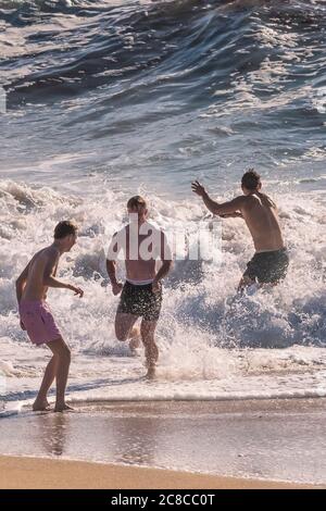 I vacanzieri maschili che corrono in mare a Fistral Beach a Newquay in Cornovaglia. Foto Stock