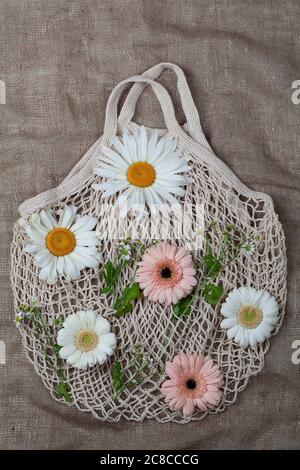 Borsa riutilizzabile in mesh di cotone bianco eco-compatibile con fiori freschi su sfondo marrone Foto Stock