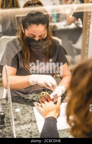 Shallow focus immagine verticale di un'artista di unghie ispanica femminile che indossa maschera pittura unghie del cliente Foto Stock