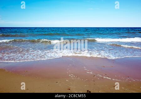 Mare calmo piccole onde che si infrangono su una spiaggia di sabbia cielo limpido orizzonte Foto Stock