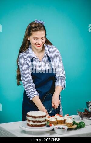 Donna di pasticceria felice in blusa spogliata che decora la torta deliziosa in panetteria Foto Stock