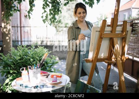 Artista femminile che usa un pennello mentre dipinge in cortile Foto Stock