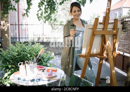 Artista femminile che usa un pennello mentre dipinge in cortile Foto Stock