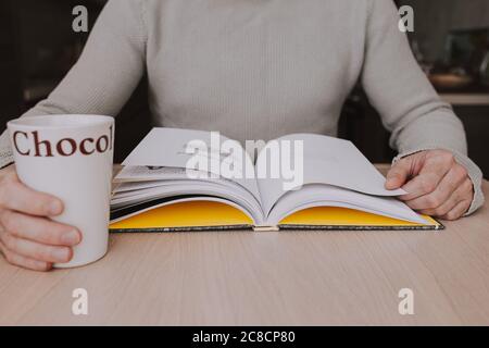 Una tazza di cioccolata calda mentre legga un libro affascinante è un passatempo favorito mentre accogliente a casa Foto Stock