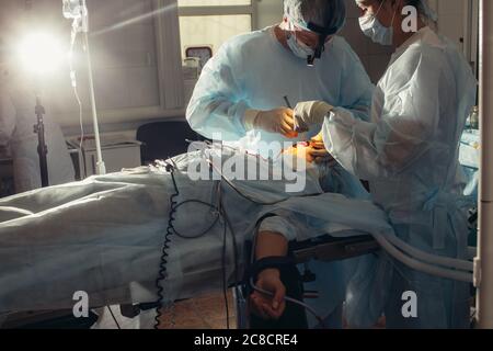 Chirurgo che esegue chirurgia estetica sul naso in sala operatoria dell'ospedale. Chirurgo in maschera indossare loupes chirurgico durante la procedura medica. Naso aumento Foto Stock