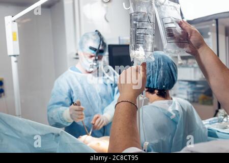 Medico la mano e gocciolamento di infusione in ospedale su sfondo sfocato Foto Stock