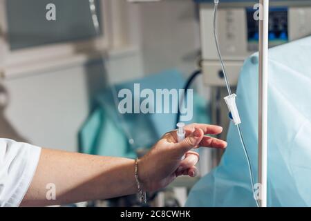 Medico la mano e gocciolamento di infusione in ospedale su sfondo sfocato Foto Stock