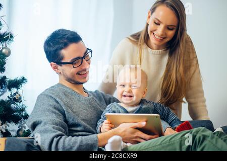 Natale mattina, allegra famiglia seduta in soggiorno divertirsi con il tablet digitale che Babbo Natale ha portato lei Foto Stock