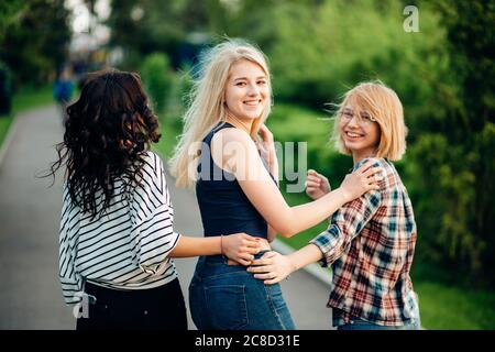 Vista posteriore di tre belle donne sedute su erba e abbracci Foto Stock