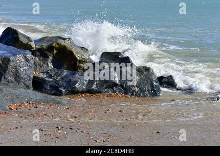 Grandi rocce su una spiaggia di pietra con onde che si infrangono contro di loro in estate. Fondo blu profondo del mare Foto Stock