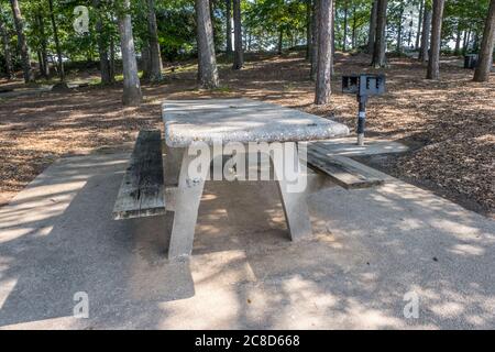 Tavolo da picnic vuoto e grigliare all'ombra non utilizzato e pulito seduto su un tappetino di cemento nel bosco in un parco in una giornata di sole in estate Foto Stock