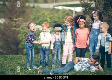 Figli di culture diverse insieme. Nel Parco su erba verde a tutta lunghezza. Il concetto di popoli, amicizia, infanzia e co interculturale Foto Stock