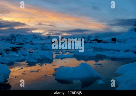 Ghiaia con la base cilena Gonzalez Videla sullo sfondo alla luce della sera, sulla terraferma antartica a Waterboat Point in Paradise Bay Foto Stock