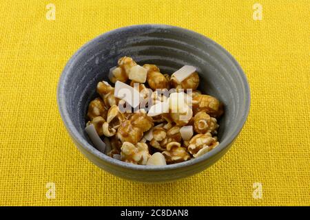 Spuntino tropicale al caramello con popcorn al cocco e pezzi di ananas essiccati in una ciotola di ceramica su tovaglia gialla Foto Stock