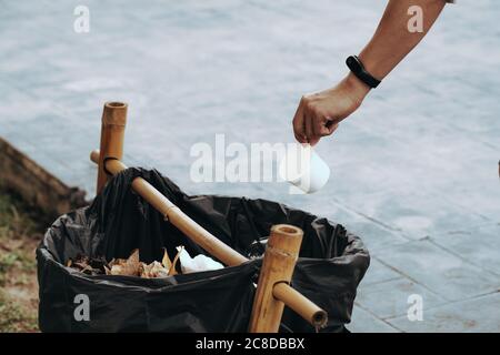 L'uomo che lancia la tazza di carta in bidone della lettiera all'aperto. Riciclaggio concetto in una giornata di sole sullo sfondo di un'erba verde. Foto Stock