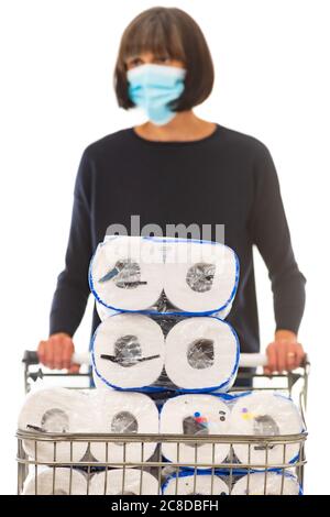 Donna che indossa maschera chirurgica spingendo carrello supermercato per lo shopping caricato con rotolo di carta igienica. Foto Stock