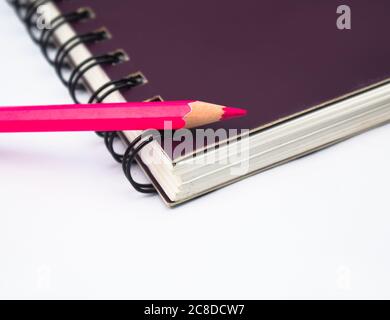 Pastello a matita di legno di colore rosa posto su una carta da libro di note a spirale di colore viola Foto Stock